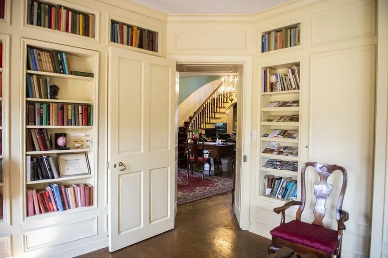 The formal library — built-in shelves, an antique chair, and a view through to the grand staircase